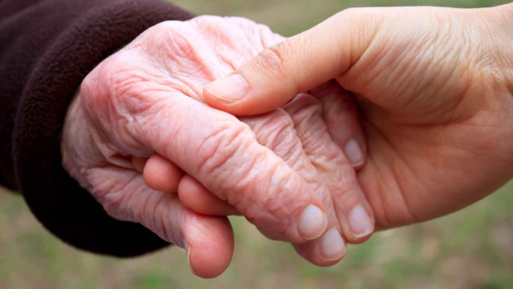 Una mano joven sostiene la de una persona mayor.
