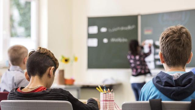 Niños de espaldas sentados atienden en clase.