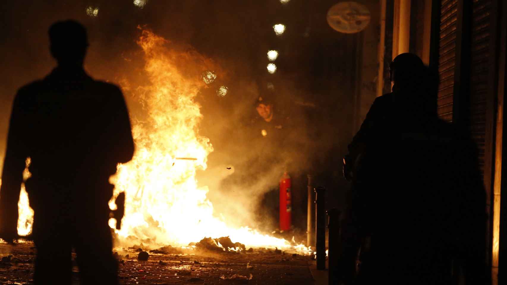 Dos personas presencia los contenedores y la basura quemados en una de las calles del barrio madrileño