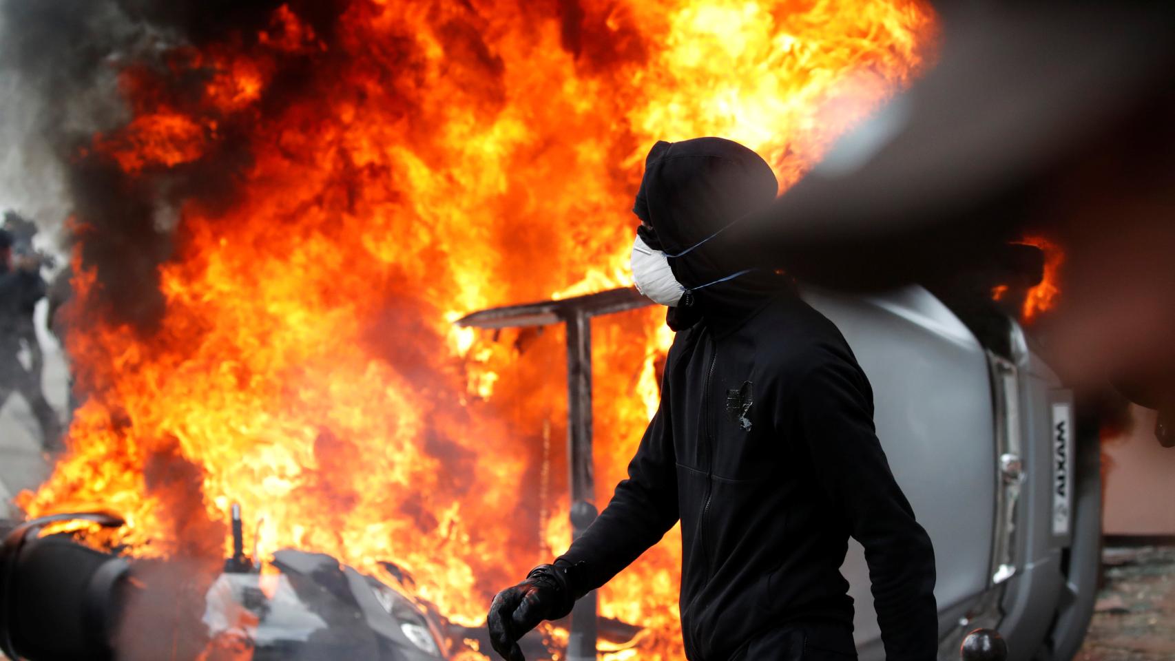 Un manifestante junto a un coche incendiado en París