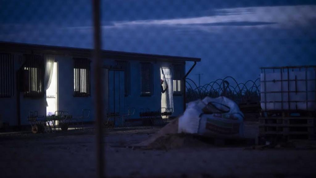 Una jornalera se asoma a la puerta del barracón en el que reside, minutos antes de comenzar su jornada laboral en una finca de fresas de la provincia de Huelva.