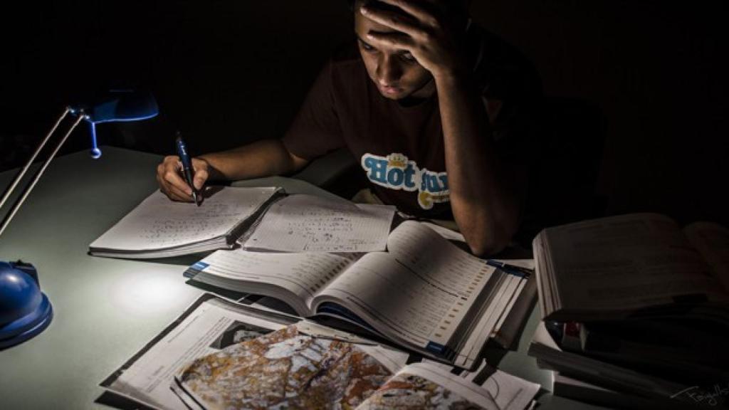 Un joven intenta estudiar ayudándose con la luz de un flexo.