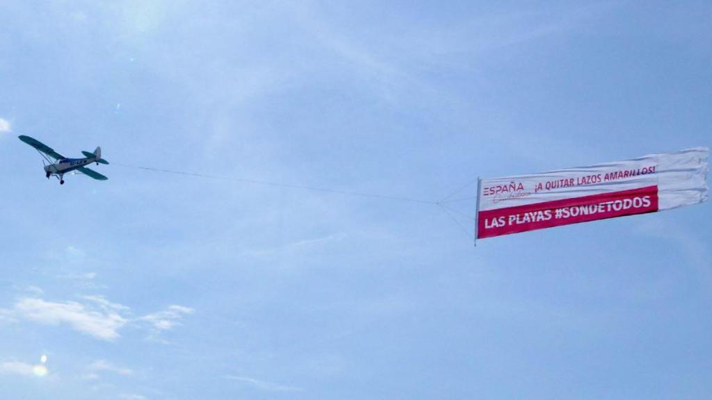 En la pancarta se puede leer: ¡A quitar lazos amarillos! Las playas son de todos