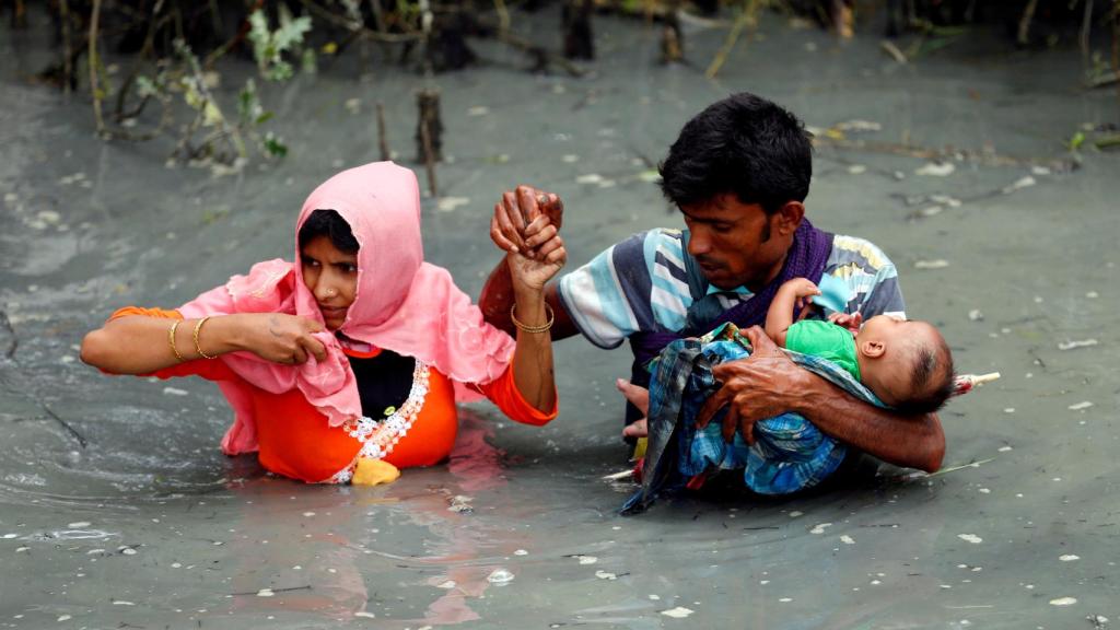 Una pareja rohingya llevan a su hijo mientras caminan a través del agua del río Naf en Teknaf, Bangladesh.