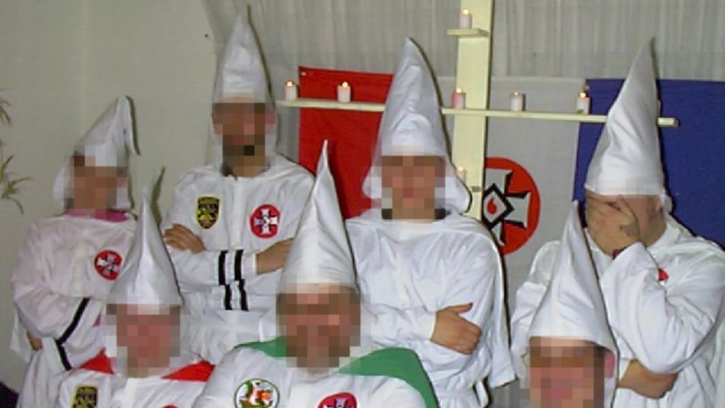 Schmid (tapándose la cara), en una reunión del KKK.