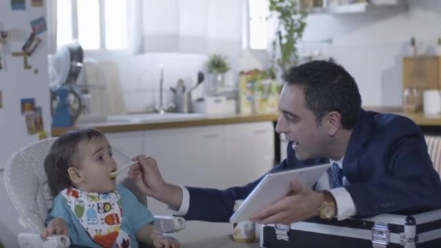 Un padre intentando dar un potito a su niño pequeño.