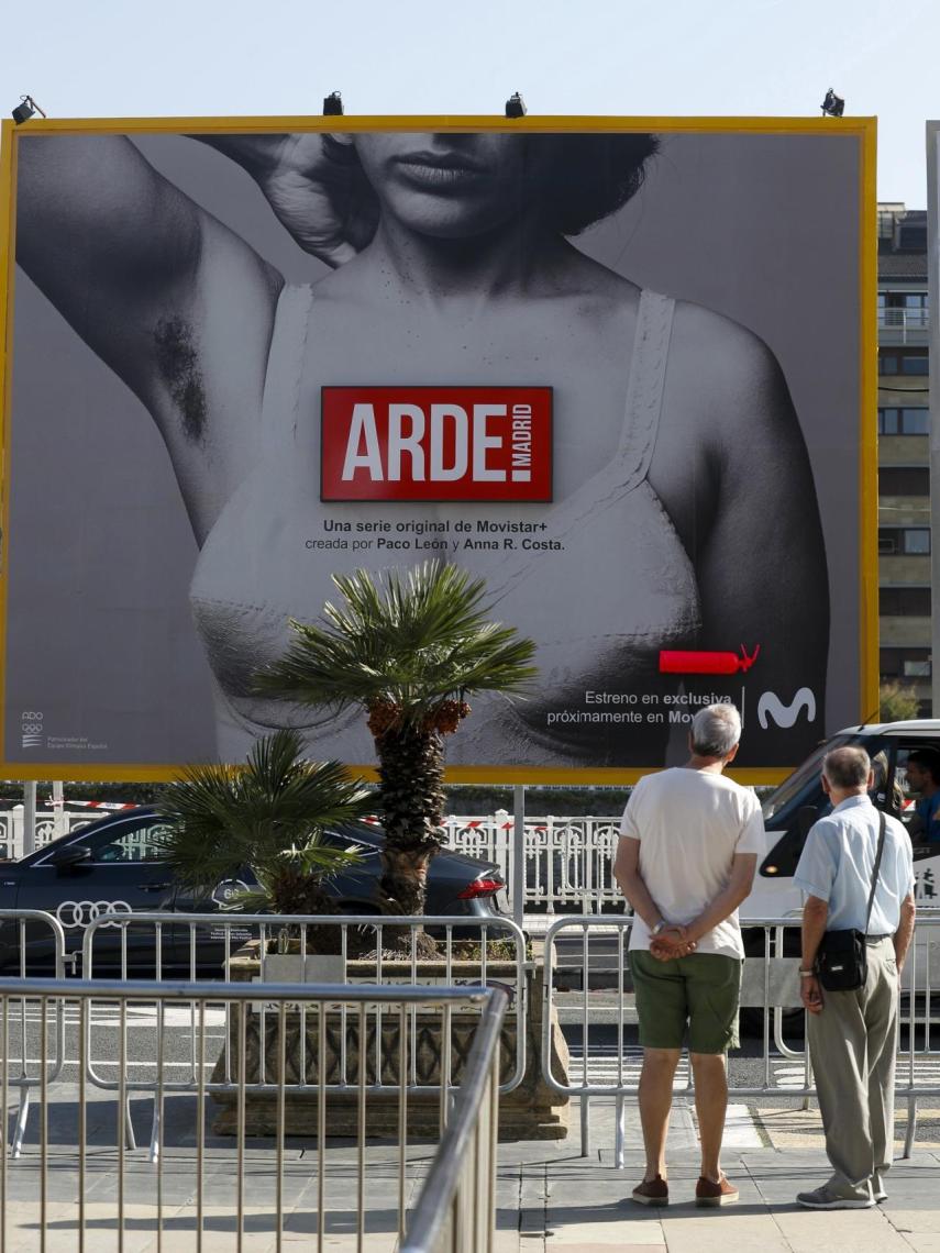 Unos hombres observan el cartel de la serie 'Arde Madrid' de Paco León.