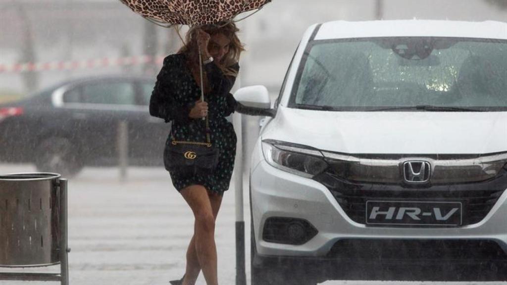 Una mujer sujeta el paraguas intentando que no se le vuele debido al viento y a la lluvia en Málaga.
