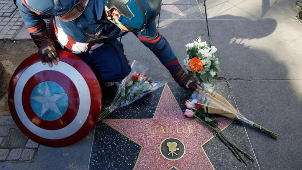 Un hombre vestido de Capitán América deja flores en la estrella de Stan Lee.