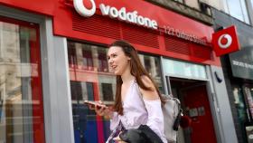 FILE PHOTO: A woman holds a phone as she passes a Vodafone  store in London