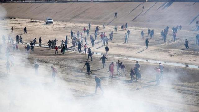 Varios migrantes de la caravana huyen del gas lanzado por la Policía de EEUU en la frontera.