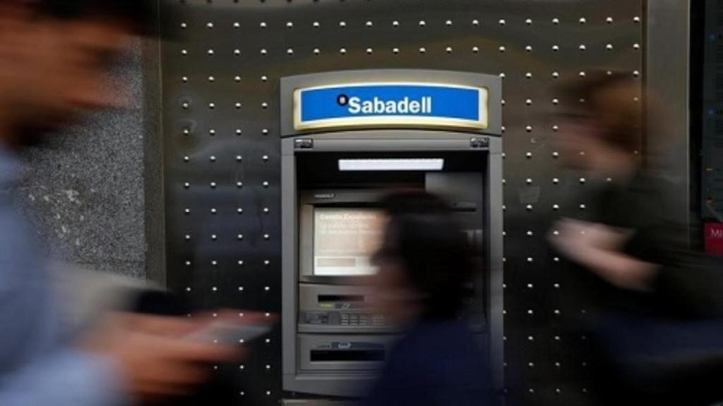 Varias personas pasan delante de un cajero de Banco Sabadell.