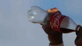 Una persona refrescándose con una botella de Coca-cola.