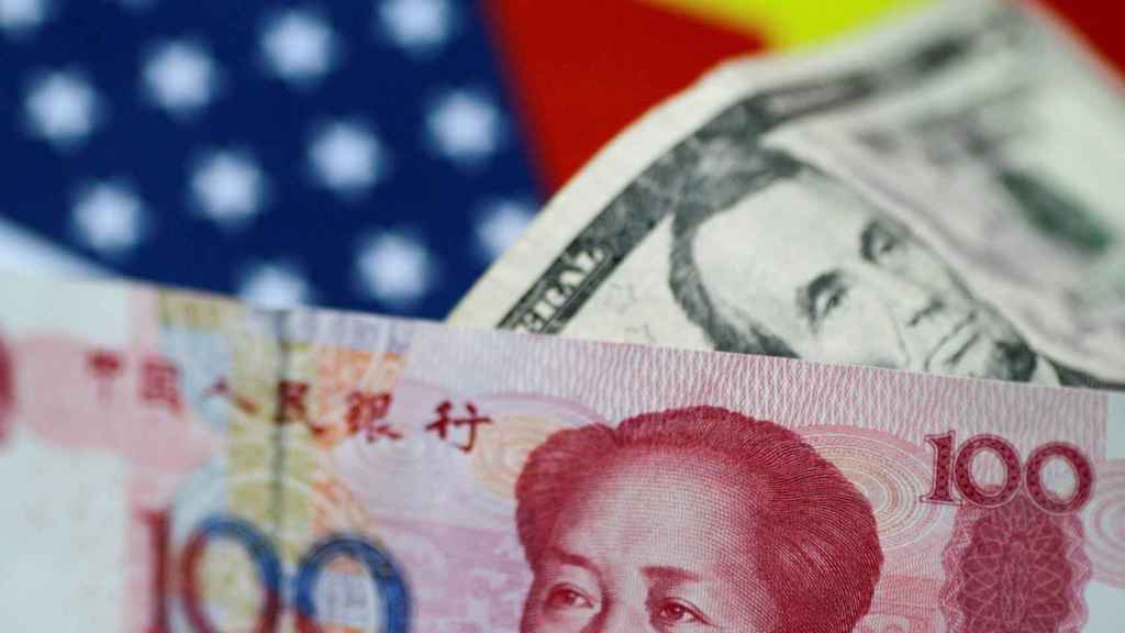 Dos billetes de yuan y dólar sobre banderas de EEUU y China.