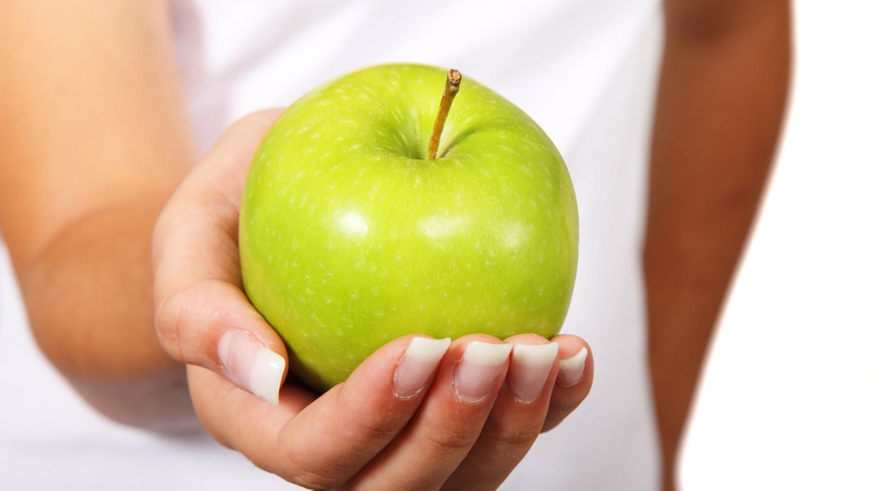 Una hermosa manzana verde que va a provocar una explosión de sabor en la boca de la mujer que la sostiene.