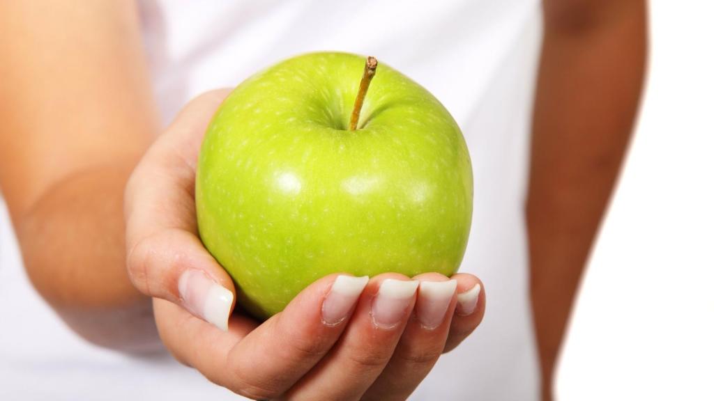 Una hermosa manzana verde que va a provocar una explosión de sabor en la boca de la mujer que la sostiene.