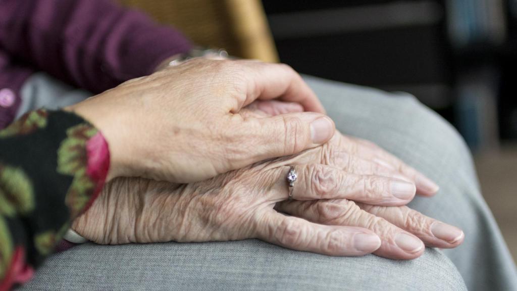 Una hija acaricia la mano de su madre anciana.