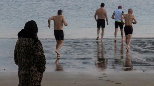 Una mujer observa a unos bañistas en la playa de Ondarreta de San Sebastián.