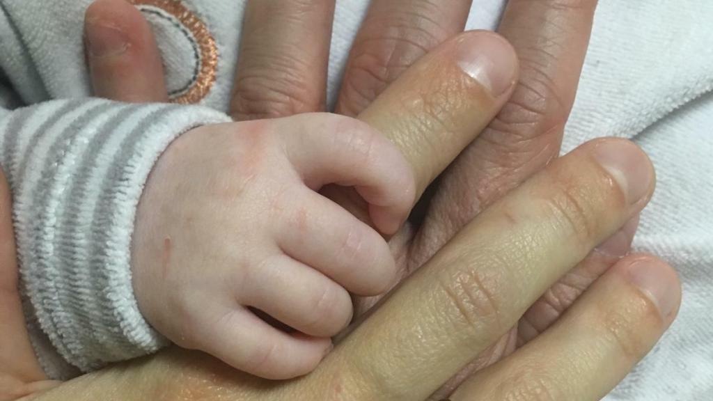 Marisol y Daniel acarician la mano de su hijo.