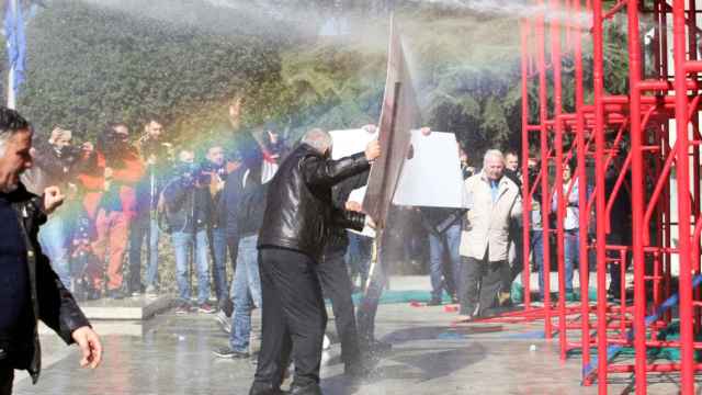 Los partidarios del partido de la oposición se protegen del cañón de agua utilizado por la policía.