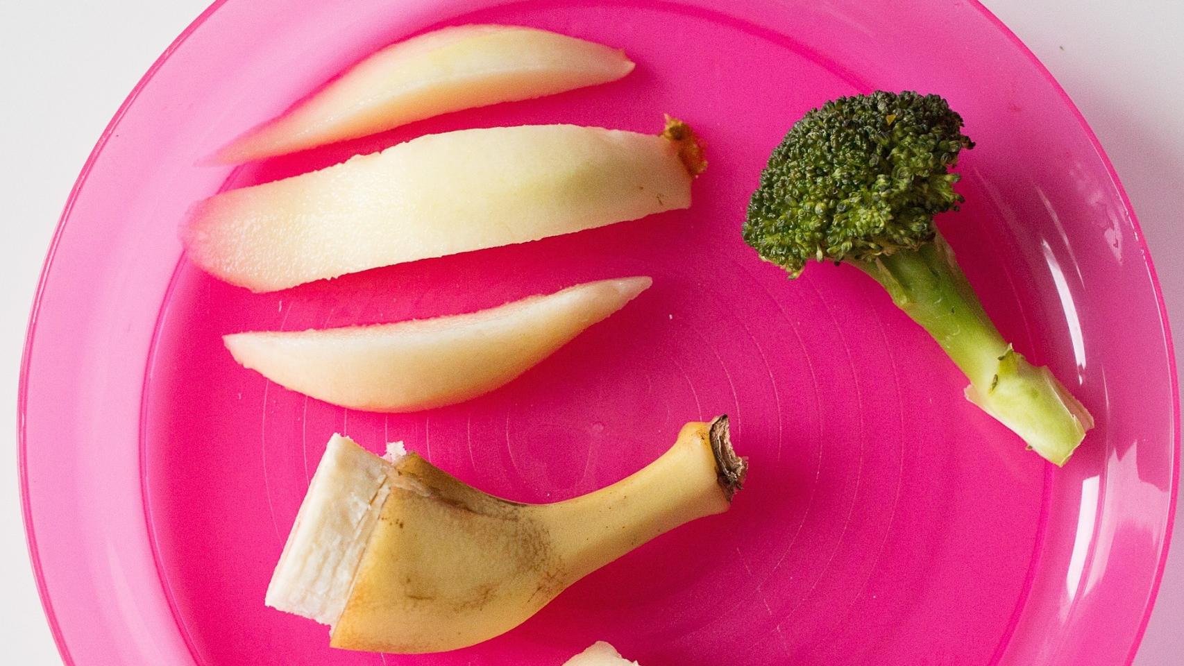 Un plato con unos trozos de manzana, brócoli y un plátano.