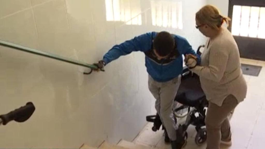 Vicenta ayudando a subir as escaleras a José Antonio, su hijo, con parálisis cerebral. Foto: Canal Extremadura