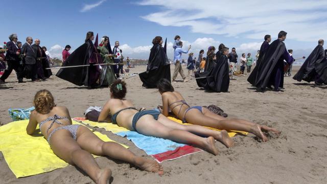 Penitentes del Santísimo Cristo del Salvador y el Amparo pasan frente a bañistas en Valencia en la Semana Santa de 2011.