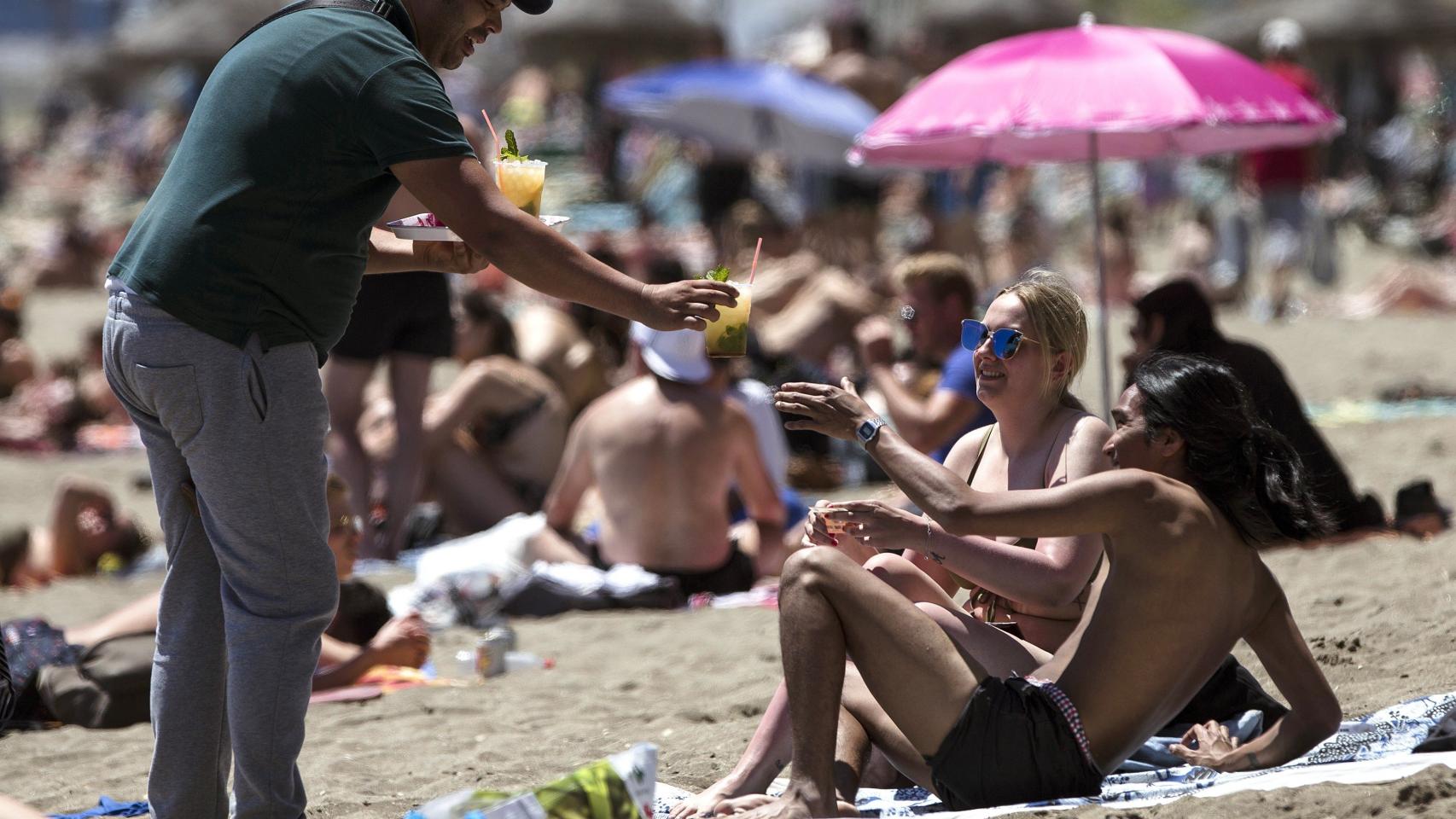 Una pareja es atendida por un vendedor ambulante en la playa de la Málagueta.