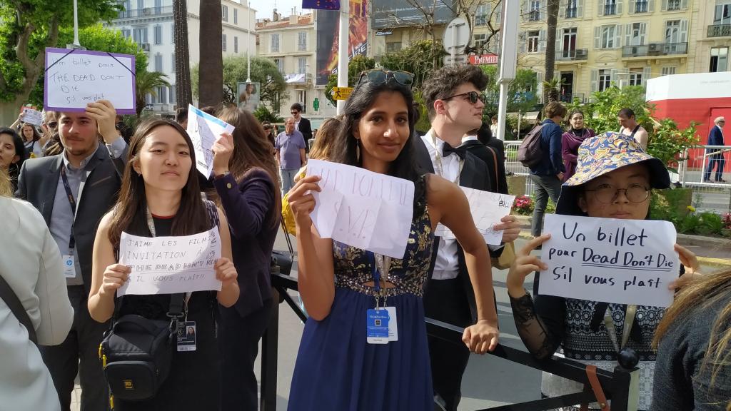 Unas chicas esperan al lado de la alfombra roja vestidas de gala y con carteles de Una entrada, por favor.