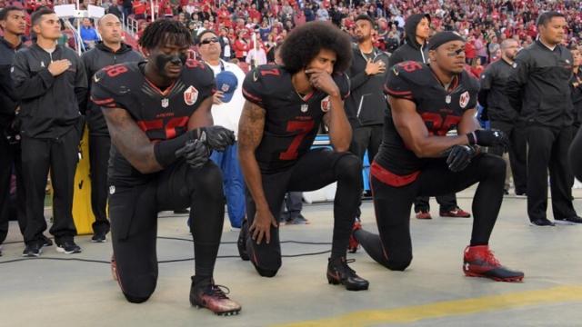 Colin Kaepernick (en el medio) arrodillado durante el himno.