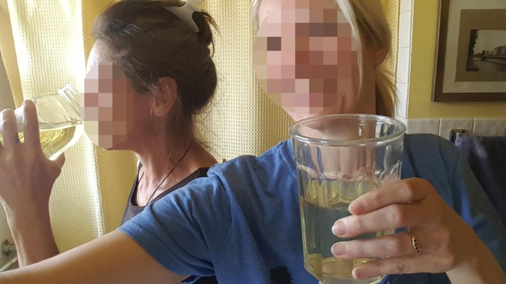 Dos amigas mostrando a cámara un vaso que contiene su propia orina.