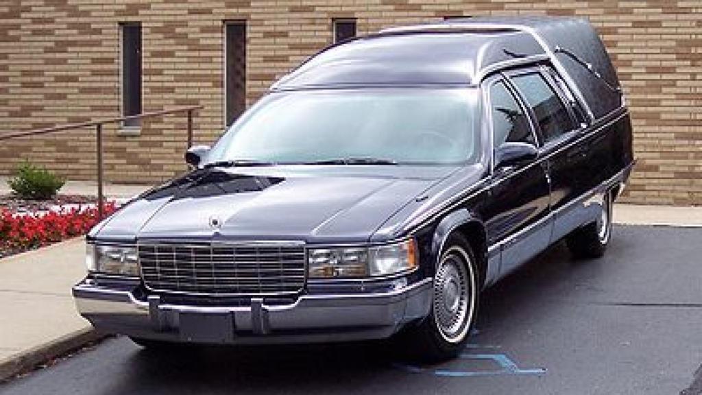 Dos empleados de una funeraria en un coche que traslada el féretro de un difunto.