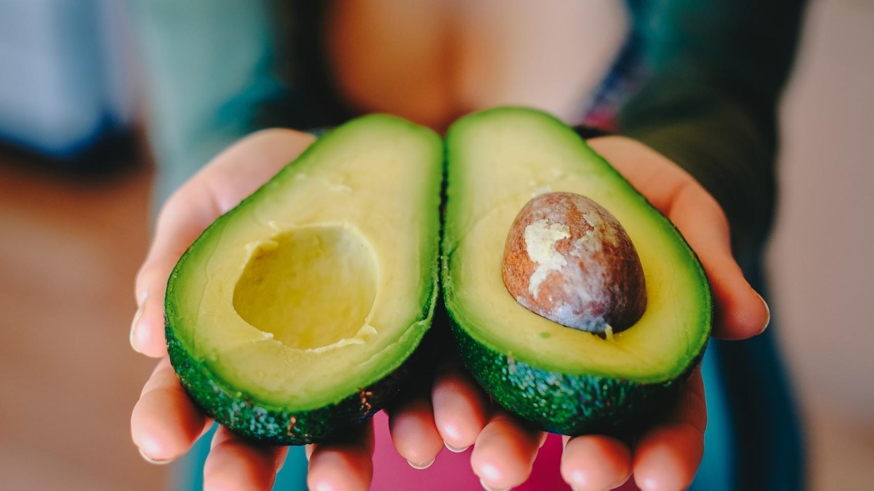 Una mujer sostiene un aguacate partido por la mitad.