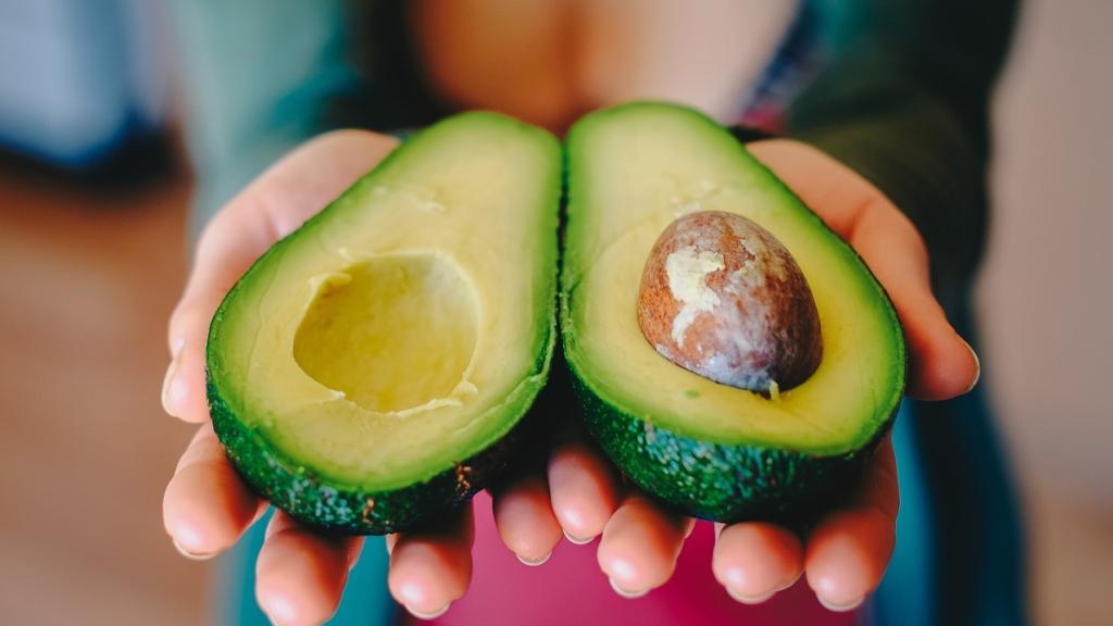 Una mujer sujeta un aguacate abierto por la mitad.