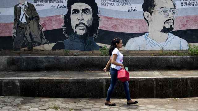 Una joven camina frente a un mural con los rostros del general Augusto C. Sandino, Ernesto 'Che' Guevara y Carlos Fonseca en la ciudad de Managua.