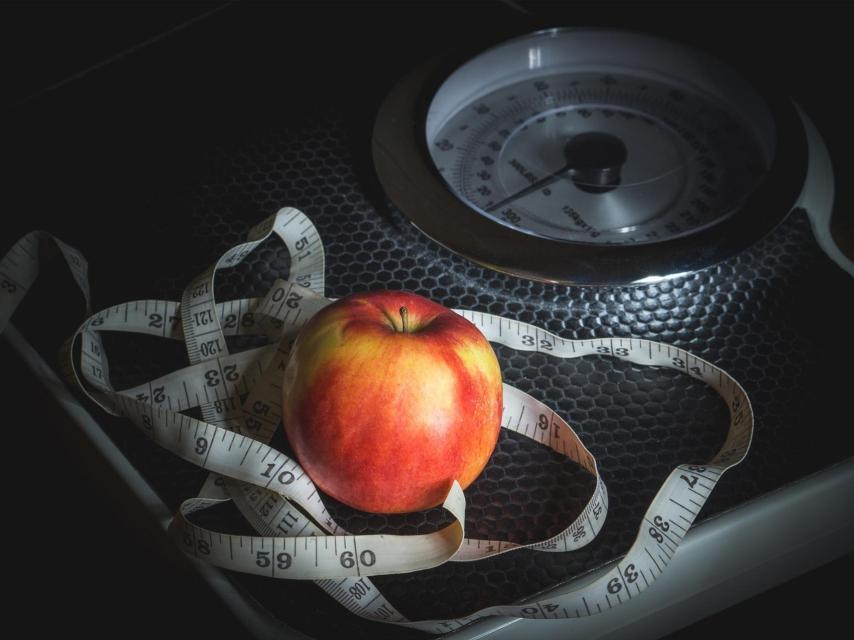 Una cinta métrica y una manzana sobre una báscula.