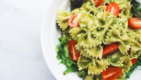 Un plato de pasta con tomatito y pesto.