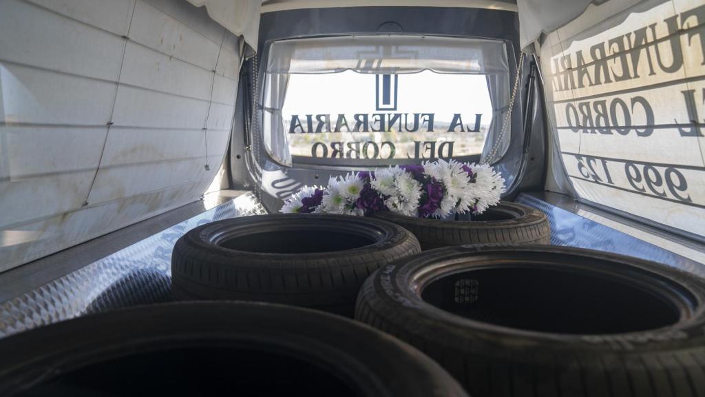 En el interior del coche fúnebre hay una corona de flores y varios recambios de ruedas.