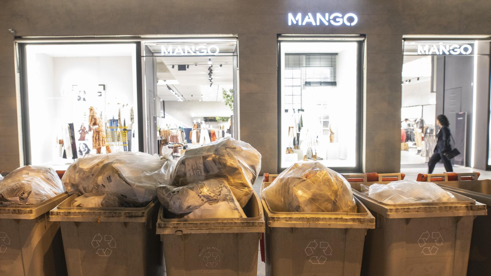 Contenedores para restos hasta arriba de plástico y papel frente a una tienda de Mango.