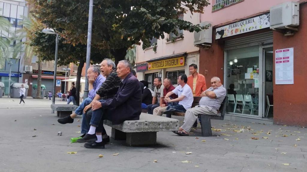 Un grupo de ancianos de origen chino pasan la tarde de este domingo en bancos de la Plaza del Reloj de Santa Coloma de Gramanet (Barcelona)