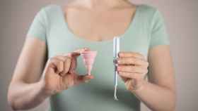 Una imagen de archivo de una mujer sujetando una copa menstrual y un tampón con aplicador de plástico.