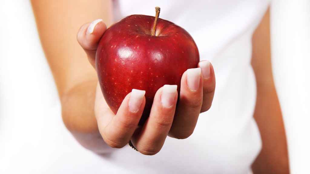 Una mujer sostiene una manzana roja con la mano.