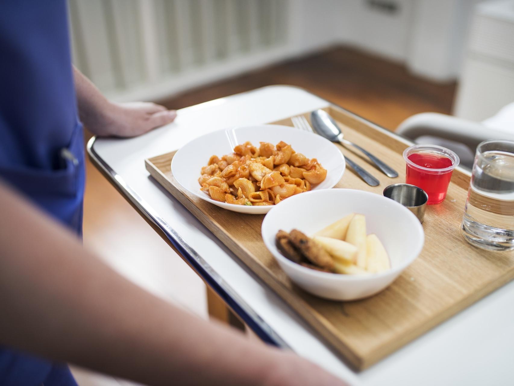 Un trabajador de un hospital lleva una bandeja con la comida de un paciente.