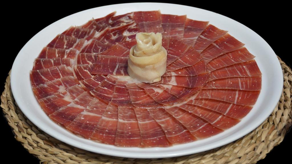 Una tabla con lonchas de jamón serrano en las que se pueden observar pequeños puntos blancos.