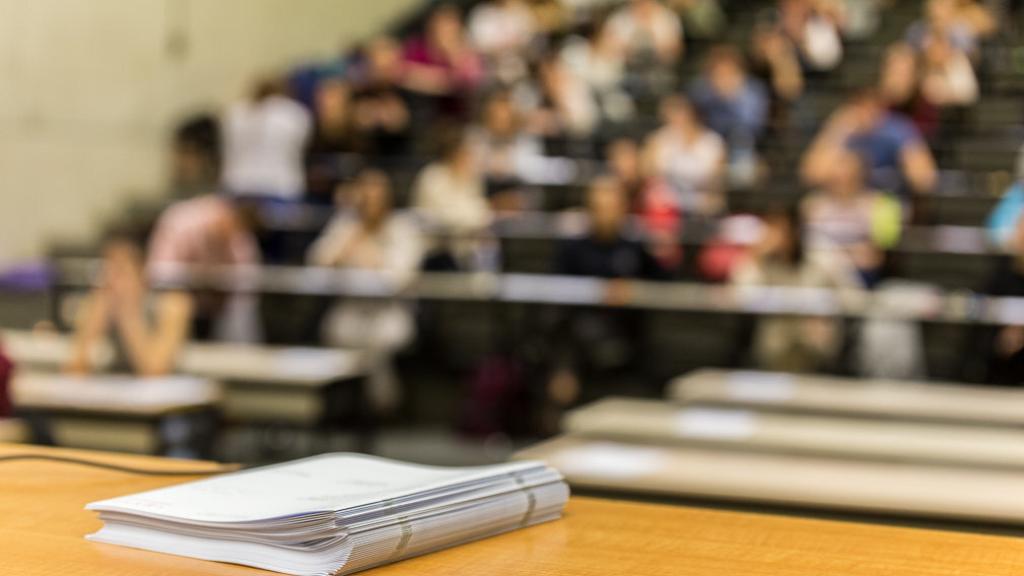 Los exámenes de EvAU sobre la mesa, mientras los alumnos que van a realizarlos esperan.