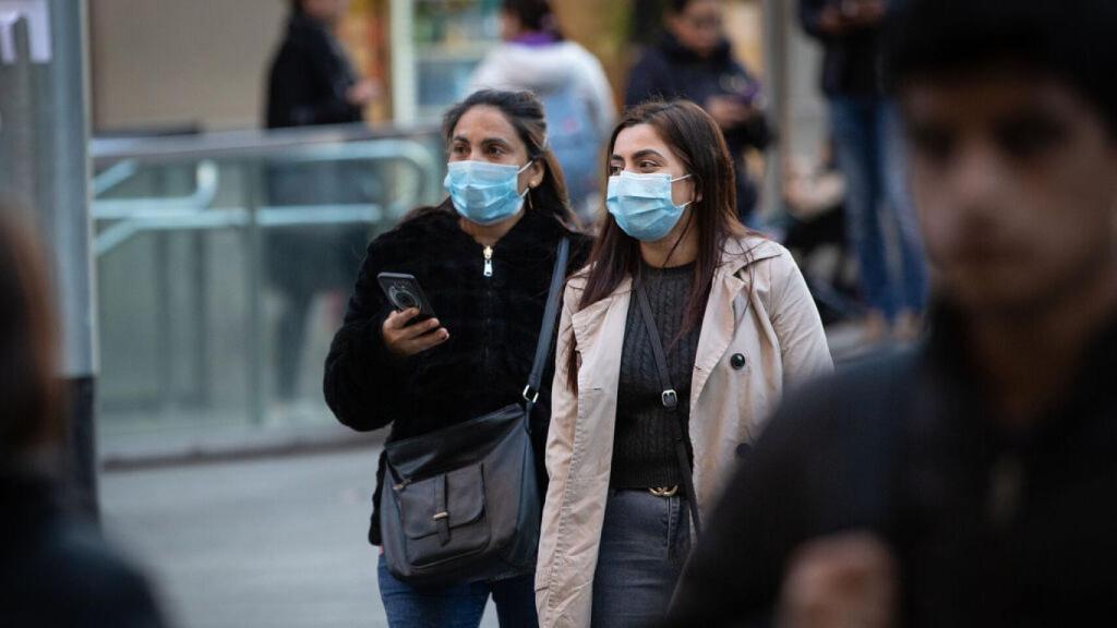 Jóvenes llevan mascarillas en una calle comercial.