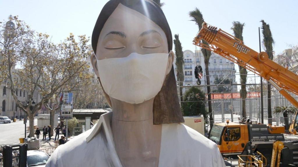 Operarios instalando una mascarilla al 'ninot' principal del monumento de la Plaza del Ayuntamiento de Valencia.