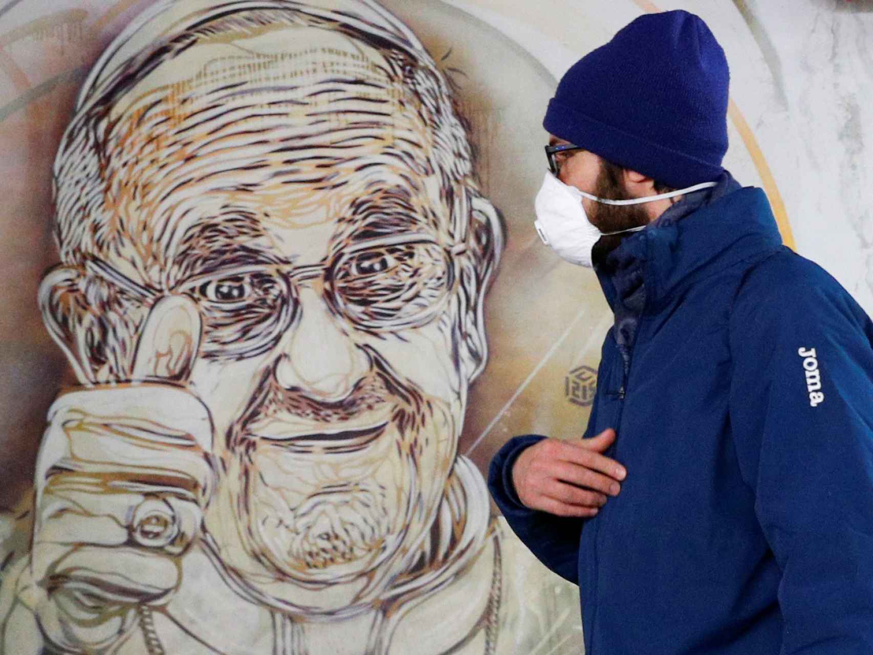 Un hombre con una mascarilla pasa por delante de un mural de Papa, en Roma.