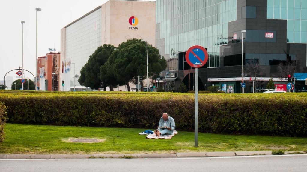 Un hombre lee el periódico en la rotonda frente a Ifema.