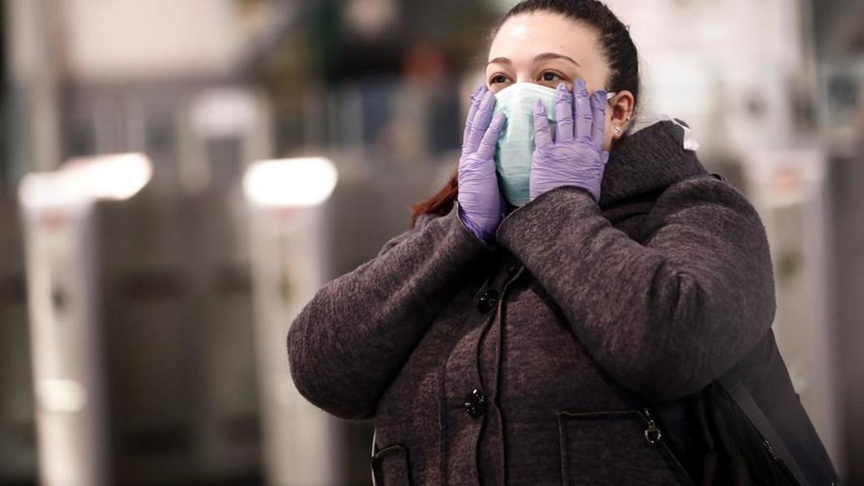 Una joven se sujeta la mascarilla con las manos.